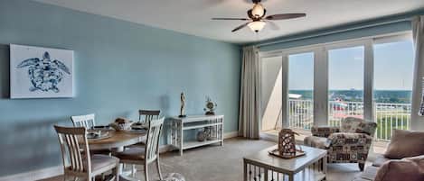 Una sala de estar con comedor, un ventilador de techo, un ventanal con vistas y una silla con temática playera.