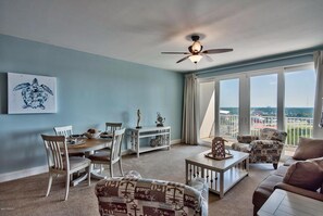 A living room with a dining area, a ceiling fan, a large window with a view, and a beach-themed chair. - Laketown Perch 1927-Lake Views-Sleeps 8 (Panama City)