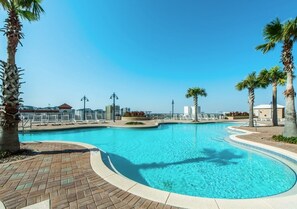 A large, clear swimming pool with a curved edge, surrounded by palm trees and a brick walkway. - Lagoon Lullaby 614-Gulf Views & Bunks-Sleeps 6 (Panama City)