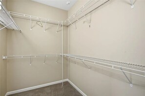 Een hoek van een kamer met een beige muur en een wit plafond. Twee witte metalen wandplanken zijn bevestigd, waarvan één met een horizontale plank en de andere met een verticale plank.