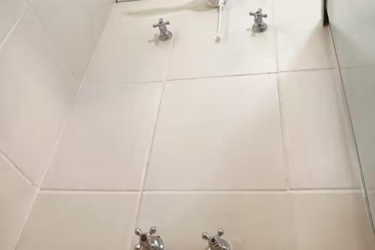 A bathroom with a shower, two faucets, and a window.