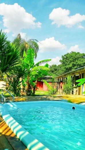 A swimming pool surrounded by lush greenery, with a clear sky above. - Suíte Acon. na Natureza - RepousaAquiÓ (Olímpia)
