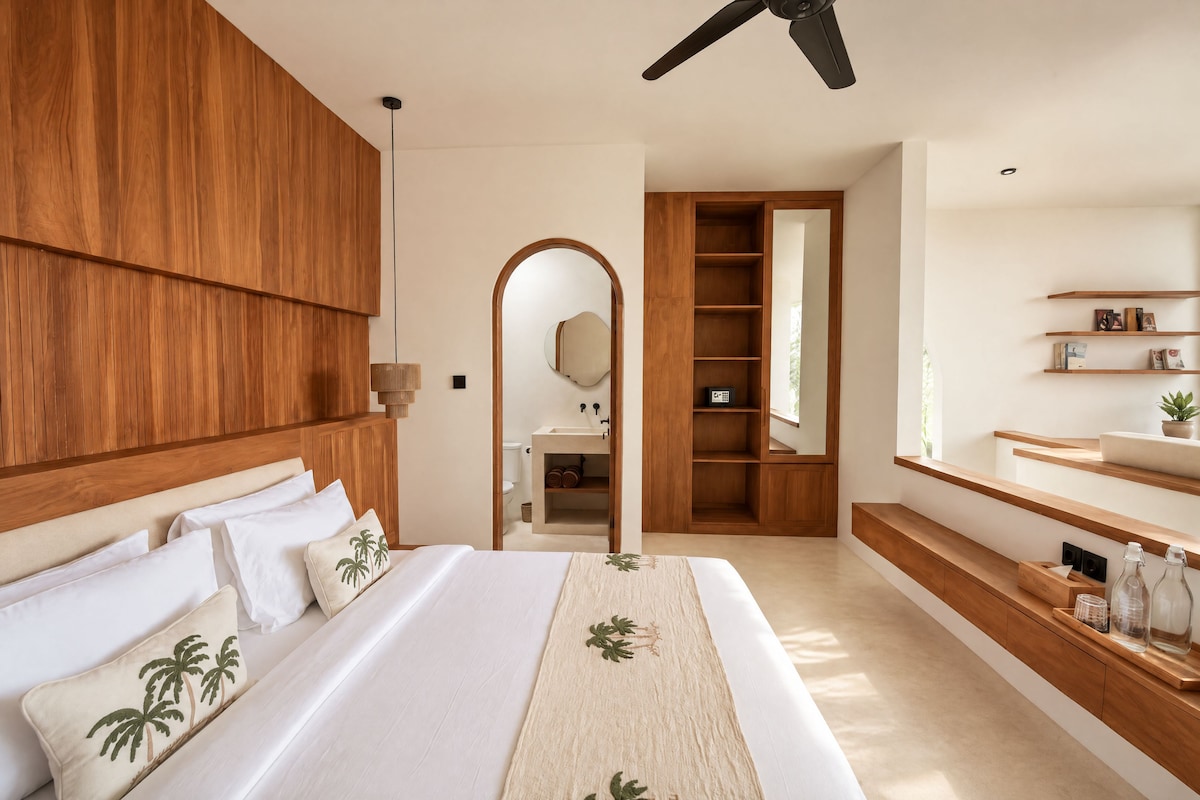 A modern hotel room with a large bed, wooden headboard, a walk-in closet, and a bathroom with a mirror and shelves.