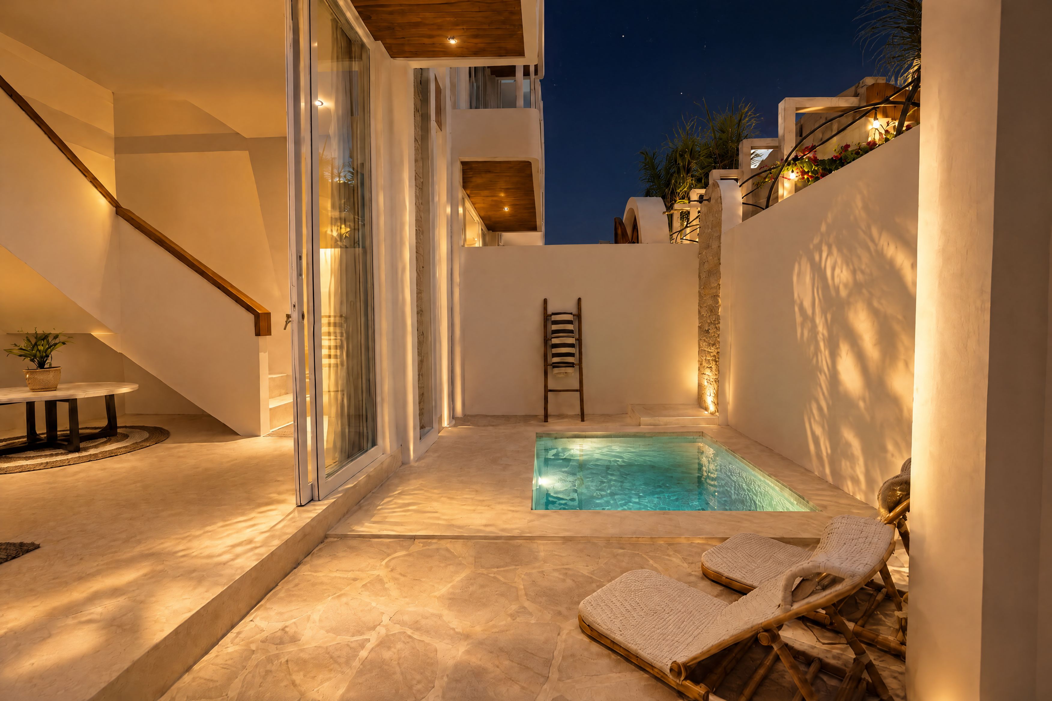 A modern outdoor pool area with a glass door entrance, a wooden staircase, and two lounge chairs.