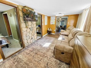 A spacious living area with a stone wall, a large sofa, and a flat-screen TV mounted on the wall. - 2BR Mercer Trailside Retreat near Turtle Flambeau with WiFi, kitchen & deck (Mercer)