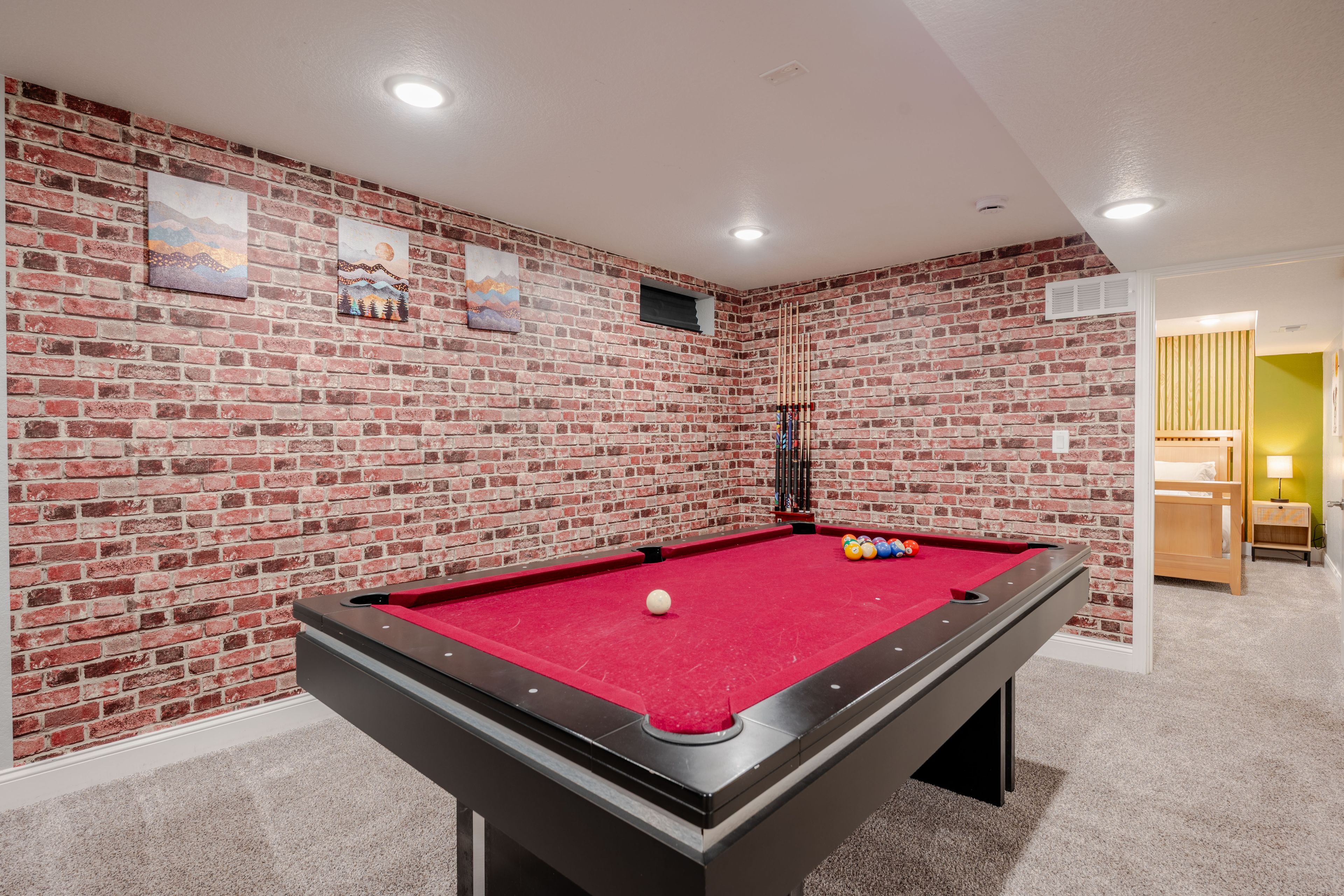 A pool table with a red felt surface, surrounded by a brick wall with artwork.