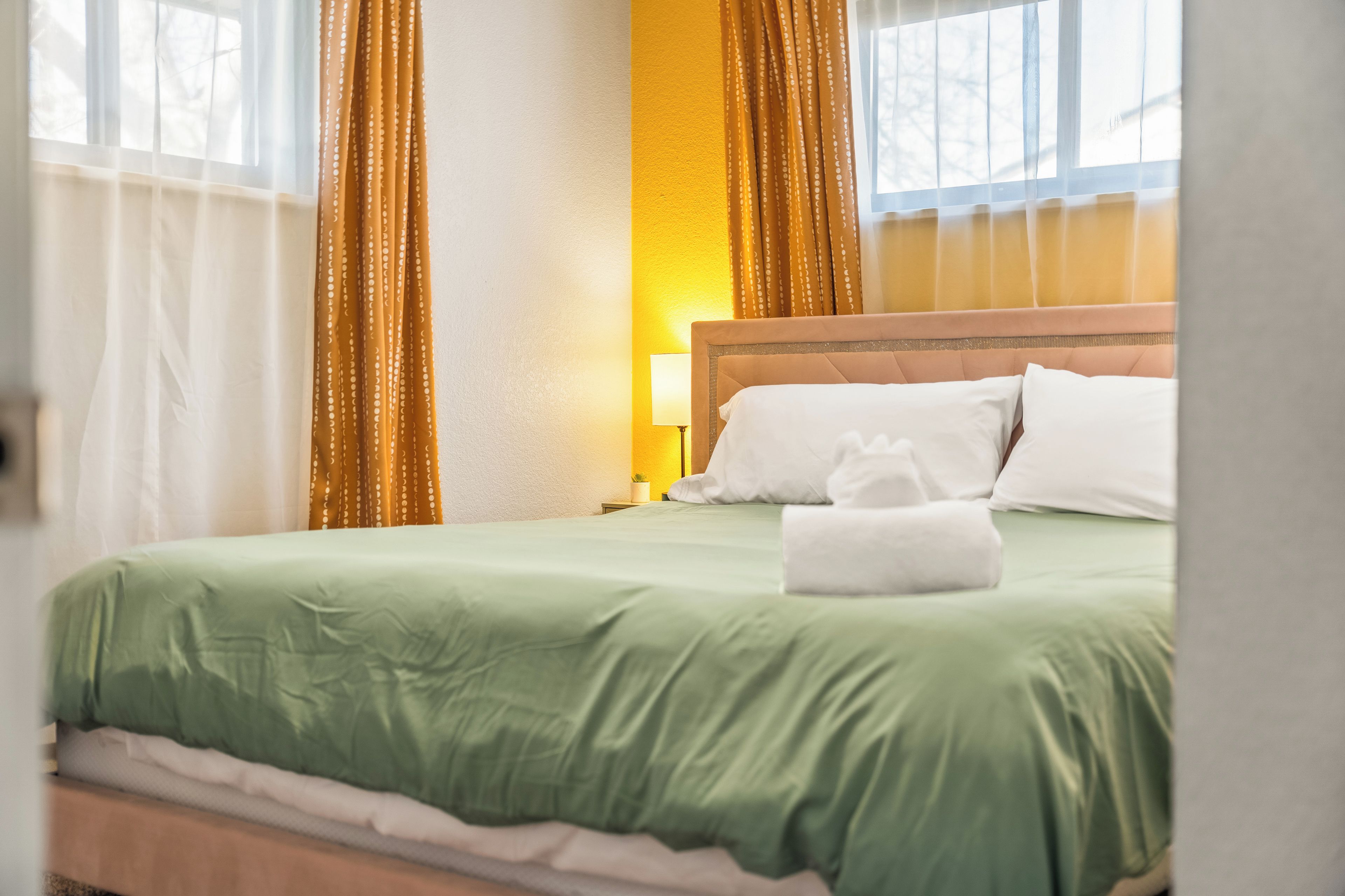 A hotel room with a bed, pillows, a bedside lamp, and curtains.