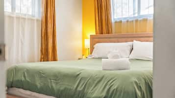 A hotel room with a bed, pillows, a bedside lamp, and curtains.