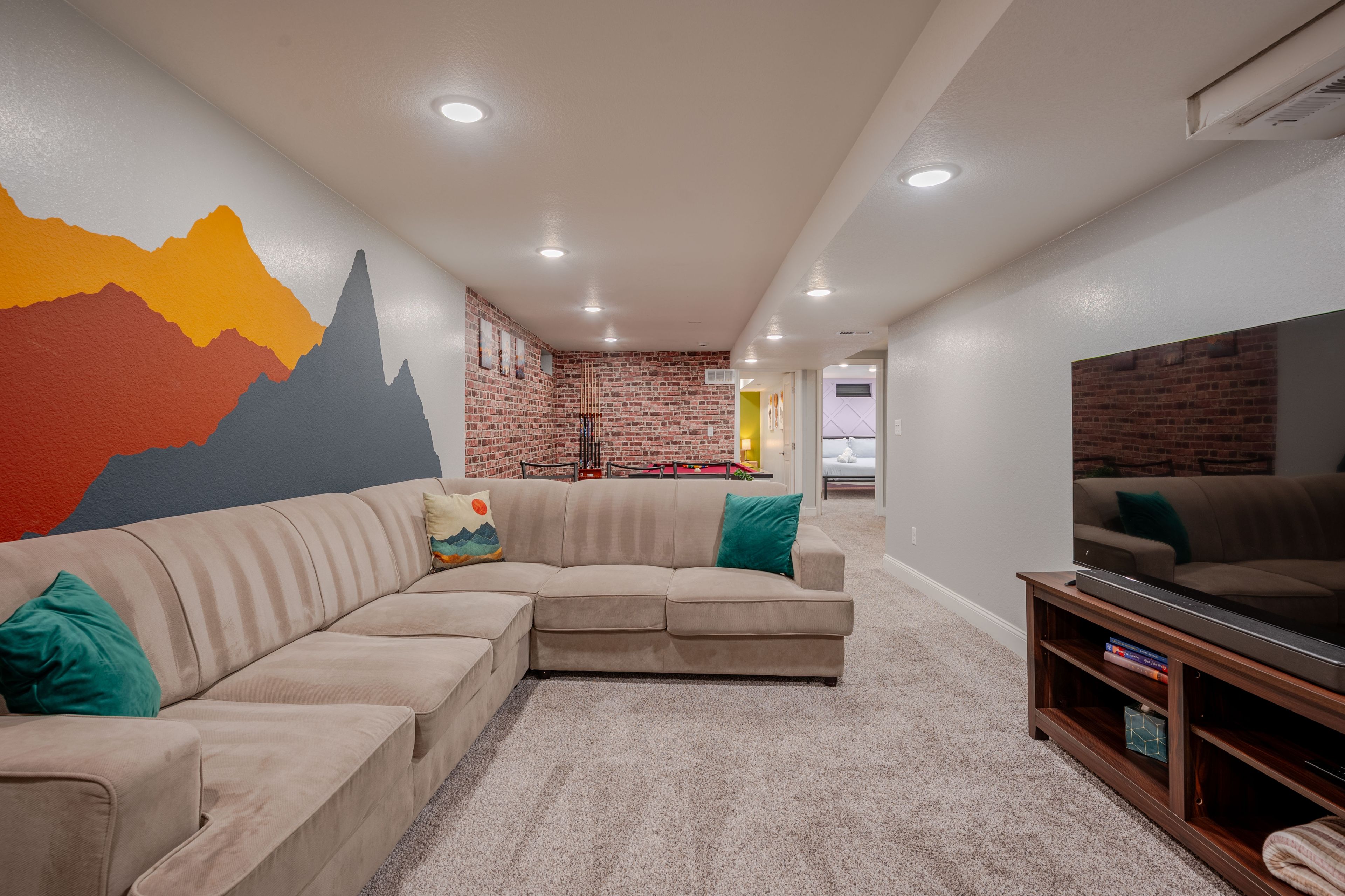 A living room with a sectional sofa, a flat-screen TV, and a brick accent wall.