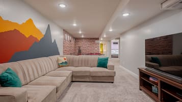A living room with a sectional sofa, a flat-screen TV, and a brick accent wall.