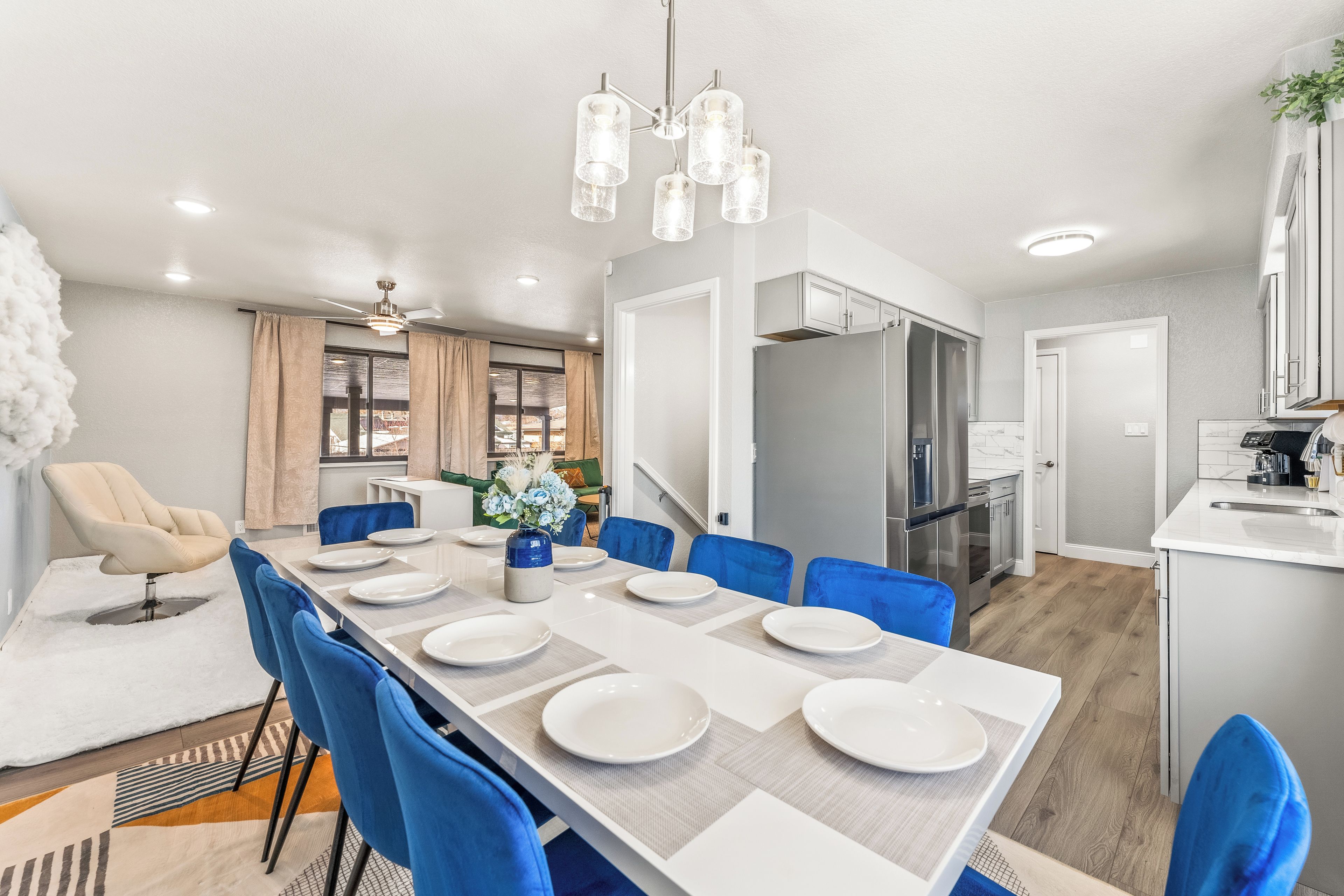 A modern dining area with a long table set for six, blue chairs, and a chandelier.