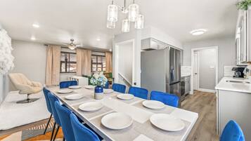 A modern dining area with a long table set for six, blue chairs, and a chandelier.