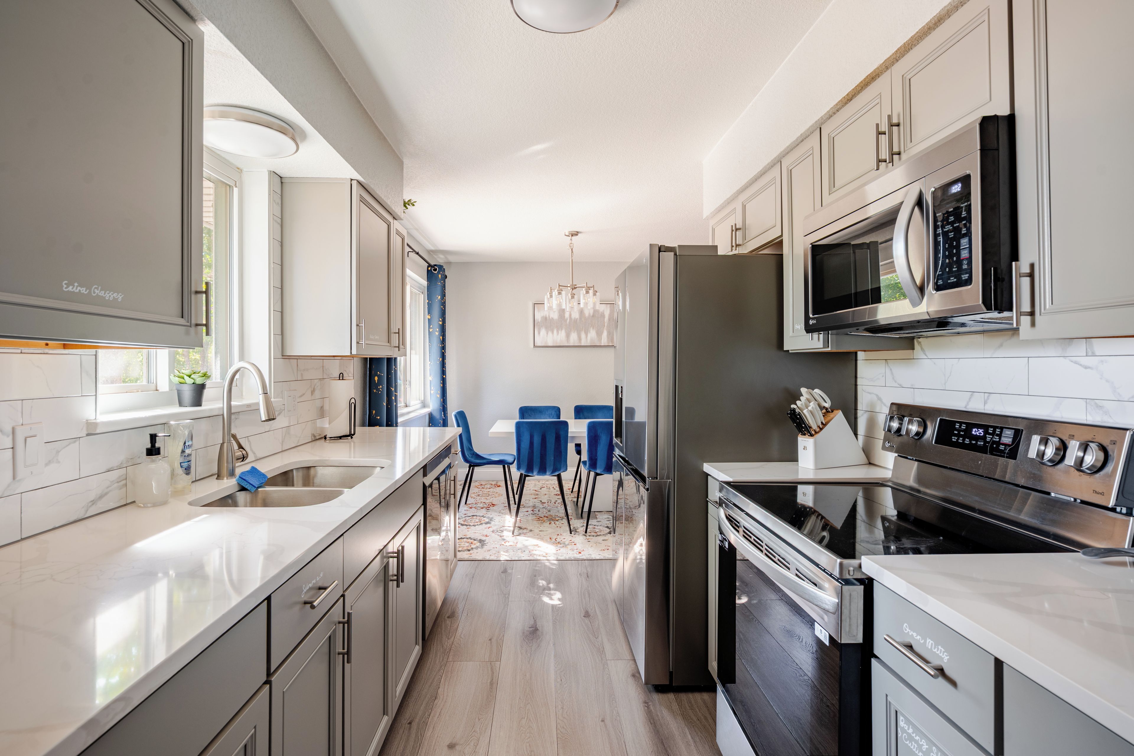 A modern kitchen with stainless steel appliances, a marble countertop, and a dining area with blue chairs.