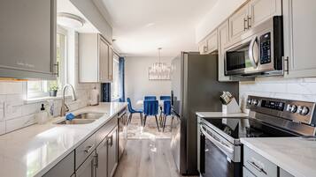 A modern kitchen with stainless steel appliances, a marble countertop, and a dining area with blue chairs.