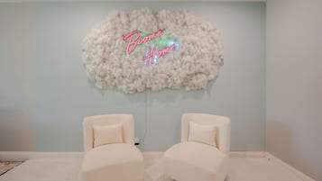 Una habitación con un adorno blanco y mullido en la pared y dos sillas blancas.