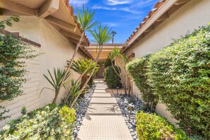A narrow pathway flanked by lush greenery and a tiled floor, leading to a building with a tiled roof. - Gorgeous Monterey Country Club Condo with Fairway Views, Covered Patio & Community Pool (Palm Desert)