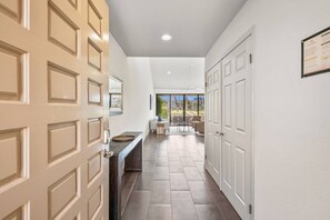 A hallway with a kitchen area, a dining space with outdoor view, and a door with a framed certificate. - Gorgeous Monterey Country Club Condo with Fairway Views, Covered Patio & Community Pool (Palm Desert)