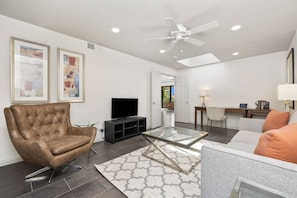 A modern living room with a leather armchair, a glass coffee table, and a flat-screen TV. - Gorgeous Monterey Country Club Condo with Fairway Views, Covered Patio & Community Pool (Palm Desert)