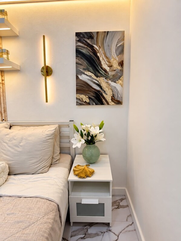 A bedroom with a bed, a nightstand with a vase of flowers, and a wall-mounted abstract painting.