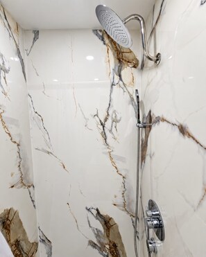 A bathroom with a shower, a wall with a marble pattern, and a chrome showerhead.