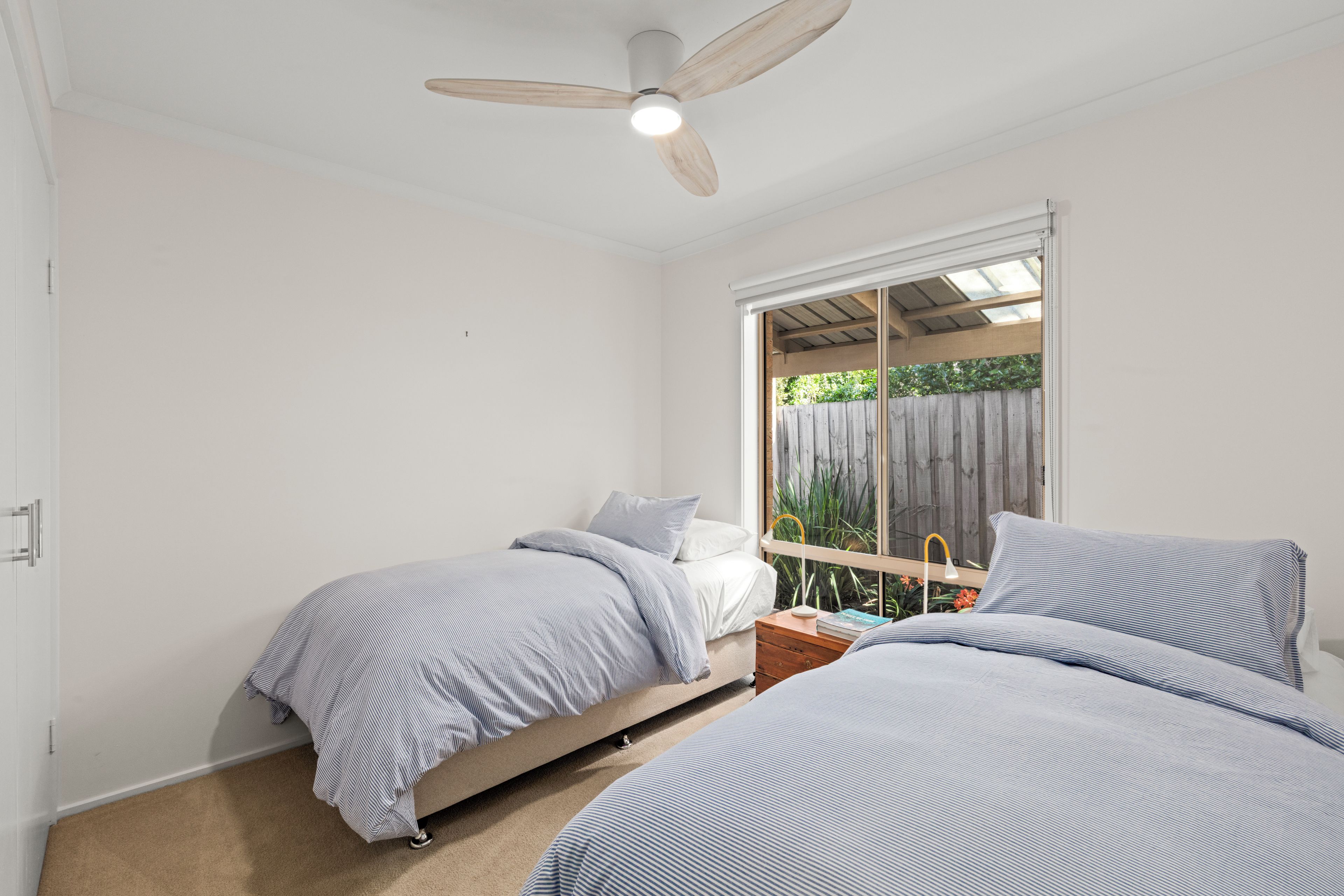 Un dormitorio con dos camas, un ventilador de techo y una ventana con vistas a follaje.