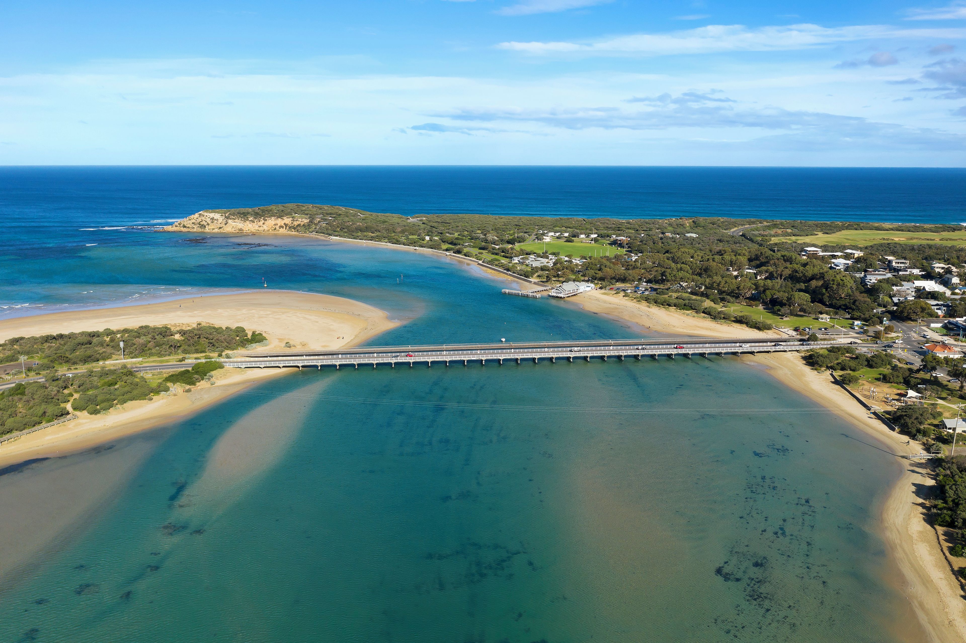 Una zona costiera con un ponte che collega due aree di terra, acque blu cristalline e una spiaggia sabbiosa.