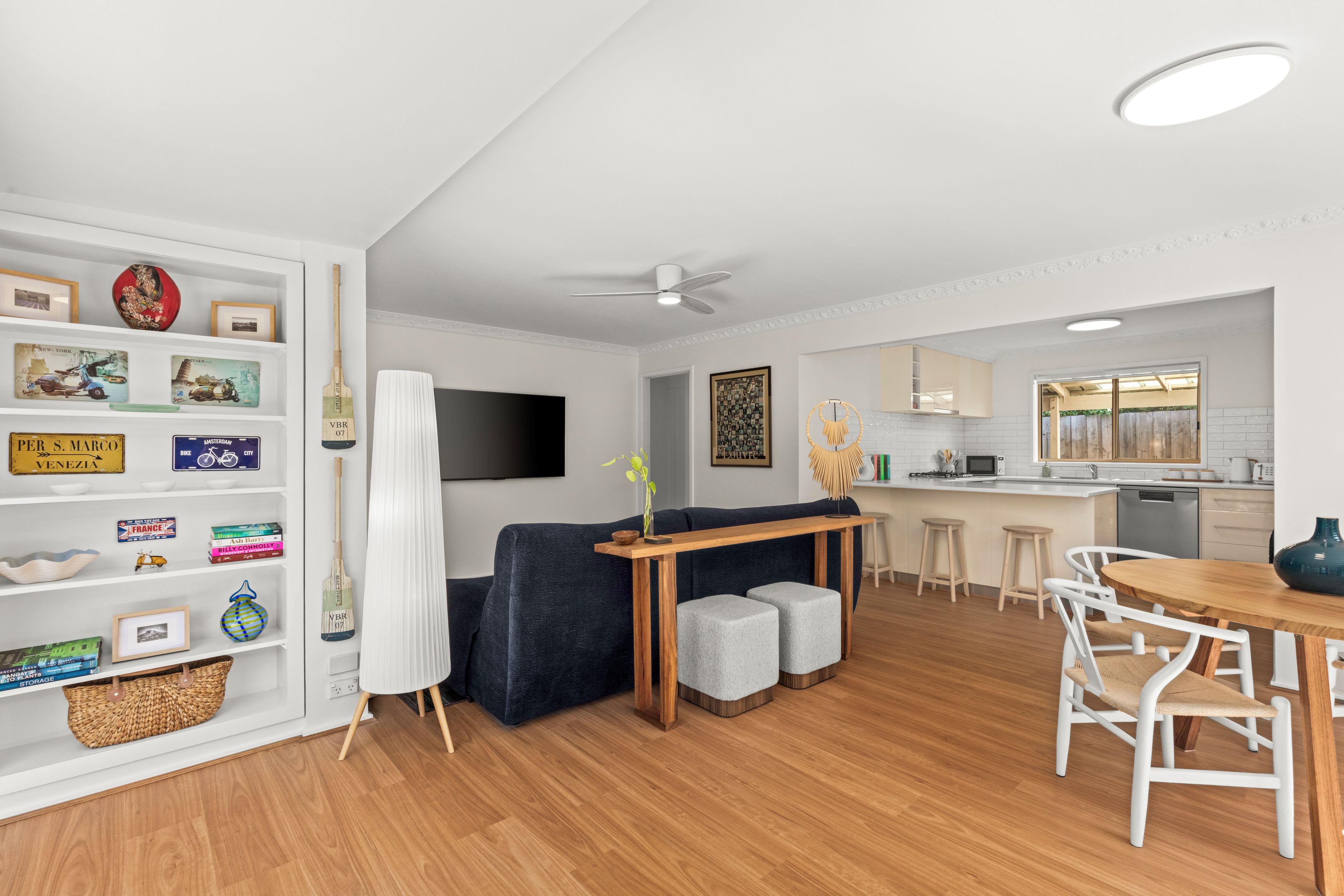 Una sala de estar moderna con un sofá azul oscuro, una mesa de centro de madera y un comedor con mesa de madera y sillas blancas.