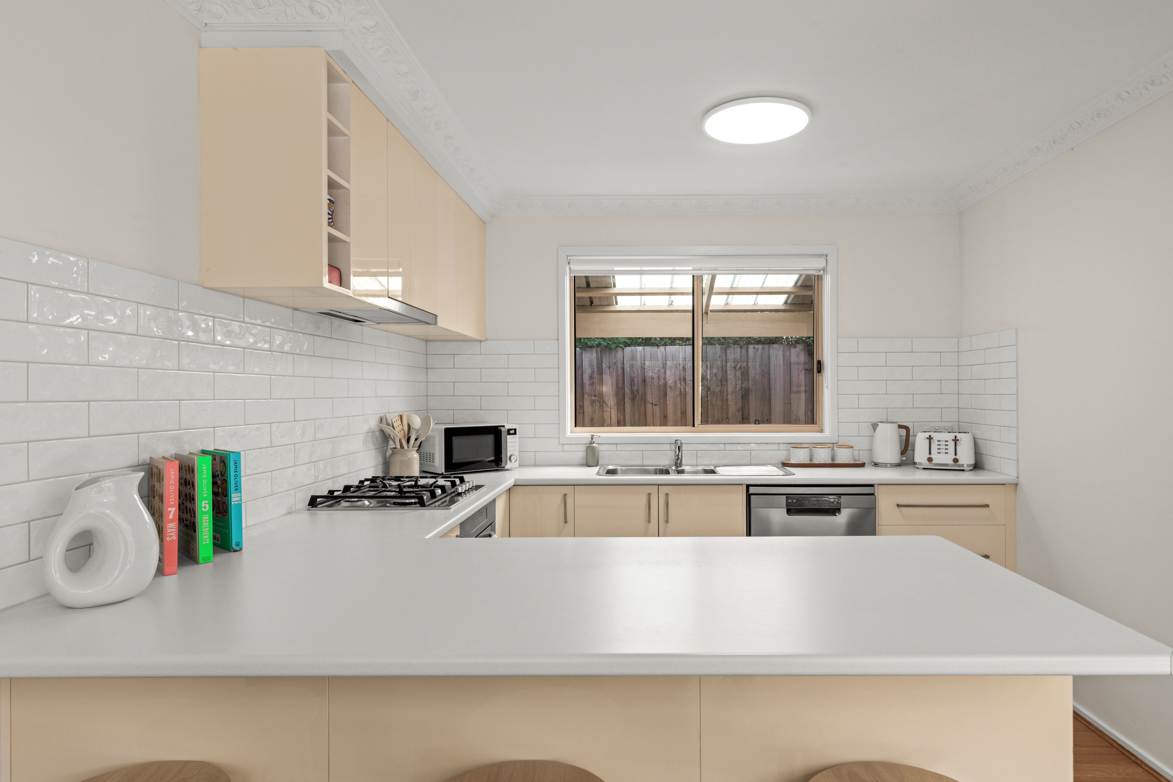 Una cocina moderna con encimeras blancas, microondas integrado, estufa a gas y armarios de madera.