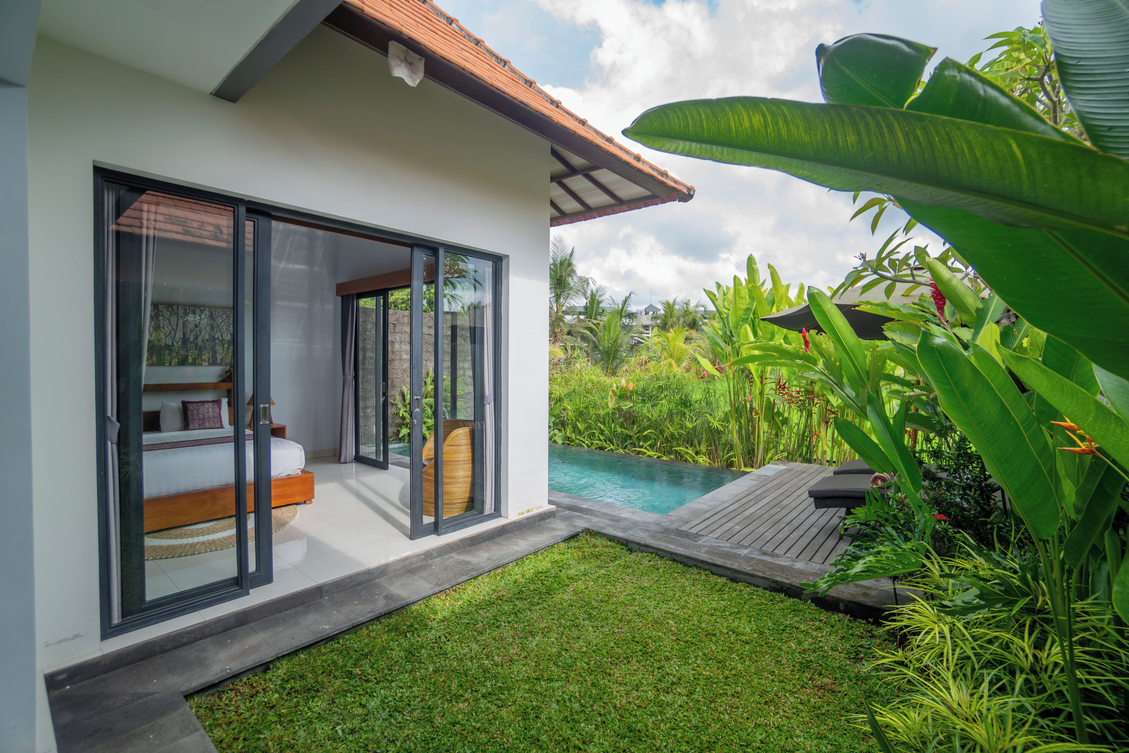 A modern house with a glass door leading to a bedroom with a bed and a window.