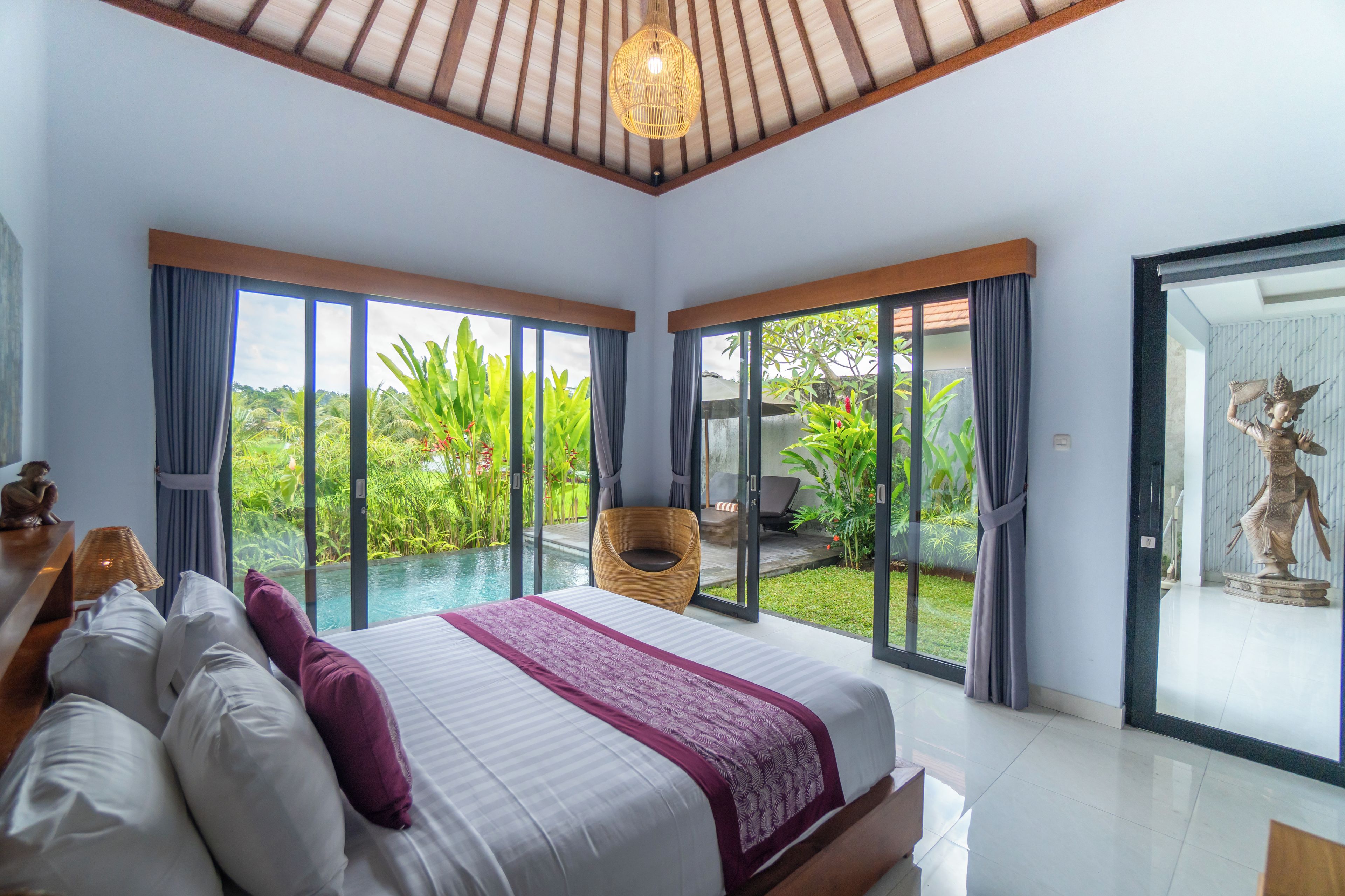 A bedroom with a large bed, a view of a pool, and a statue.