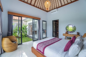 A bedroom with a bed, a chair, a mirror, and a view of an outdoor garden. - Private Pool Villa in Ubud –  Rice Paddy View, 1 Bedroom (Gianyar)