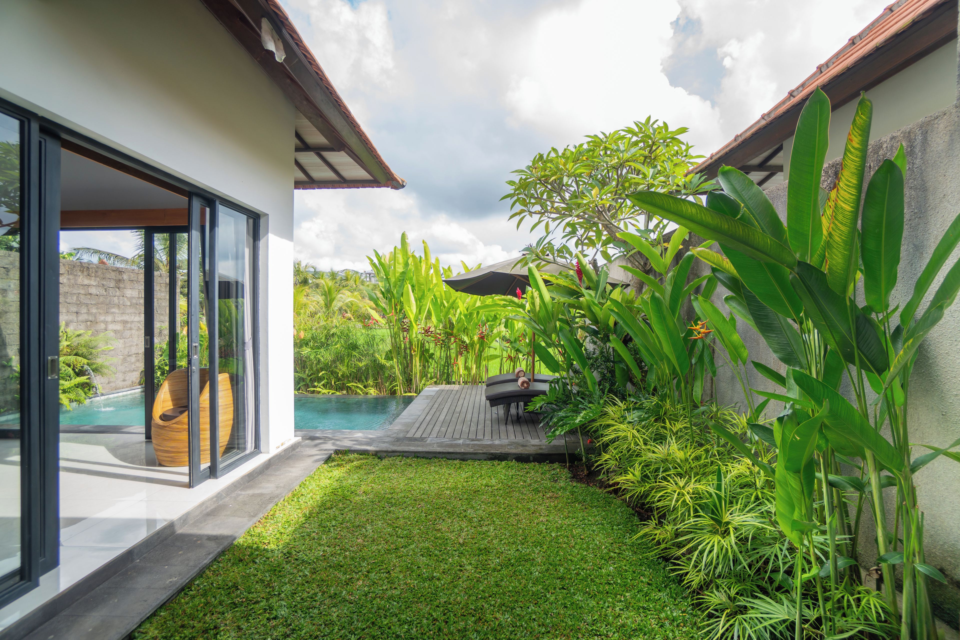 Una casa moderna con puerta de vidrio que da a una piscina, rodeada de vegetación exuberante y una terraza de madera.