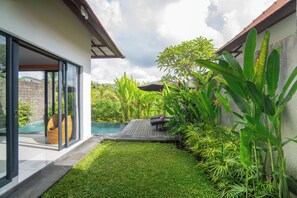 A modern house with a glass door leading to a pool, surrounded by lush greenery and a wooden deck. - Private Pool Villa in Ubud –  Rice Paddy View, 1 Bedroom (Gianyar)