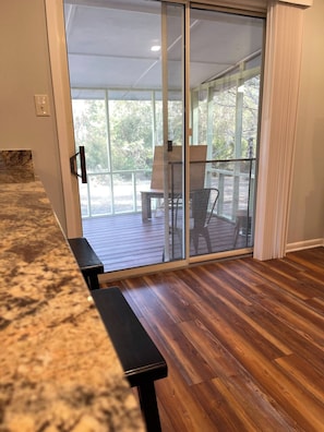A room with a wooden floor, a bench, a sliding glass door leading to an outdoor area with chairs and a table. - 20 Acre Ranch - 40 min to 30A! (DeFuniak Springs)
