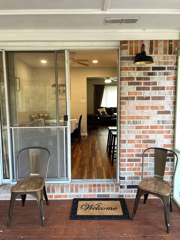 A room with a sliding glass door leading to a dining area, a brick wall, and a welcome mat.