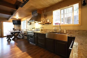 A kitchen with a large island, wooden cabinets, a stove, and a window providing natural light. - Secluded Writer's Retreat | Trails Out the Door (Pollock Pines)