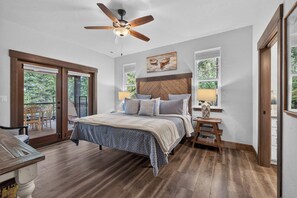 Una camera da letto con un letto, una ventola a soffitto, un comodino e una finestra vista alberi.