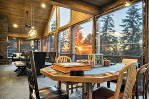 Un'accogliente zona pranzo con un grande tavolo di legno, sedie e vista su una foresta tramite ampie finestre.