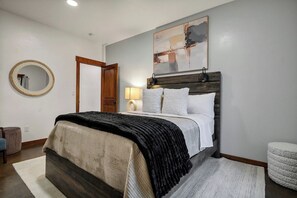 A bedroom with a bed, a round mirror, a door, a wall-mounted artwork, and a bedside lamp. - Sasquatch Lodge: Private Pool, Spa & Stargazing Dome (Coeur d'Alene)