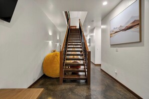 A modern interior with a wooden staircase, a large yellow bean bag, and a framed abstract painting on the wall.