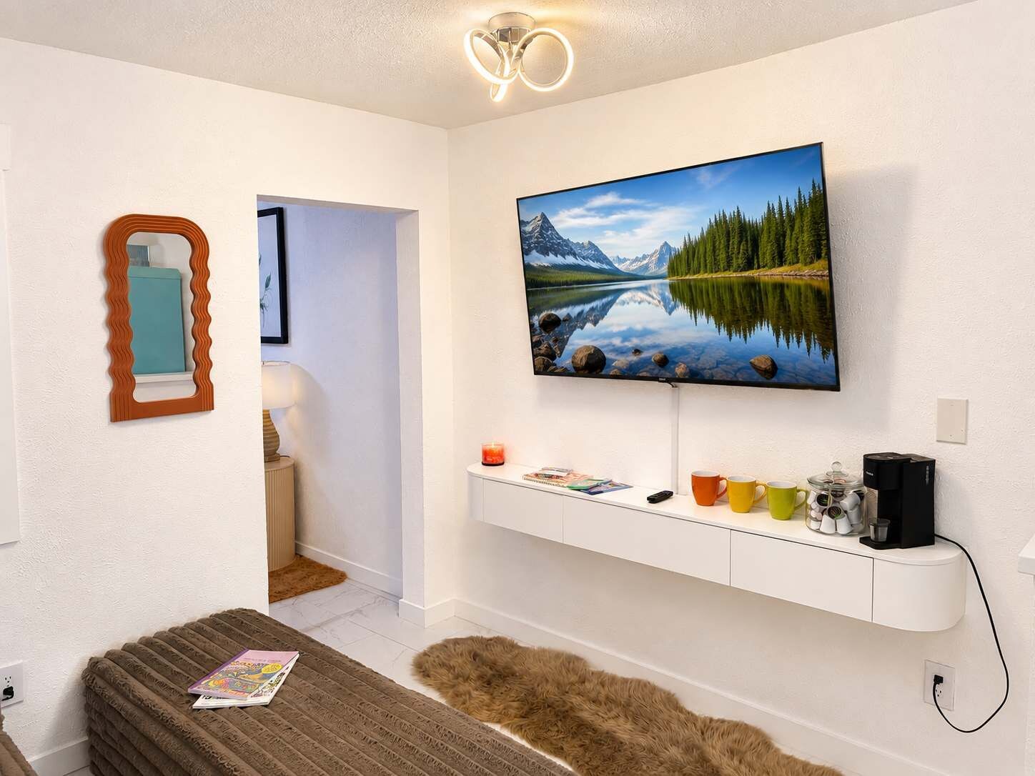 A modern living room with a flat-screen TV mounted on the wall, a cozy seating area with a brown sofa, and a white entertainment unit below the TV.