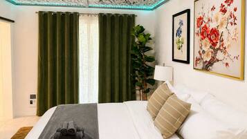 A hotel room with a bed, green curtains, a plant, and two framed floral paintings.
