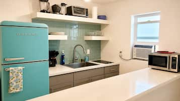 A kitchen with a teal refrigerator, a sink, a microwave, and a window.