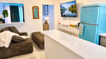 A modern kitchen with a blue refrigerator, a white countertop, and a large window with curtains.