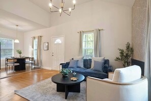 A spacious living room with a sofa, coffee table, and a dining area with chairs. - Heart ATL– 2BR/ Monthly Stays /Pet-Friendly (Atlanta)
