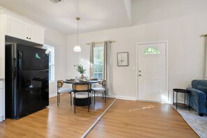 A modern kitchen with a black refrigerator, dining table with chairs, a hanging light fixture, and a door with a window view. - Heart ATL– 2BR/ Monthly Stays /Pet-Friendly (Atlanta)