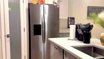 A modern kitchen with a stainless steel refrigerator, a countertop with a sink, and a door leading to another room.