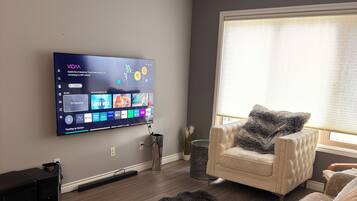 A modern living room with a flat-screen TV mounted on the wall, a sofa, a furry rug, and a window with blinds.