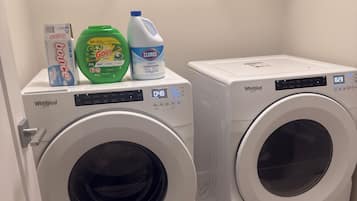 Due lavatrici Whirlpool a carica frontale in una lavanderia con uno scaffale metallico sopra pieno di detersivi.