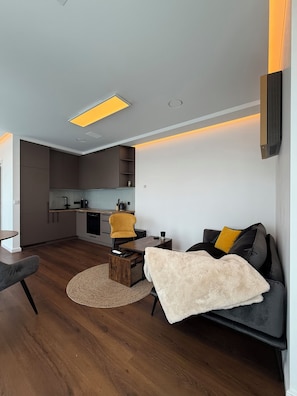 A modern living room with a sofa, a coffee table, and a kitchen in the background. - Luxury 2-Bedroom Apartment with Sonos Sound, Wi-Fi, TV, and LED Lighting in Kaunas, Freda (Kaunas)